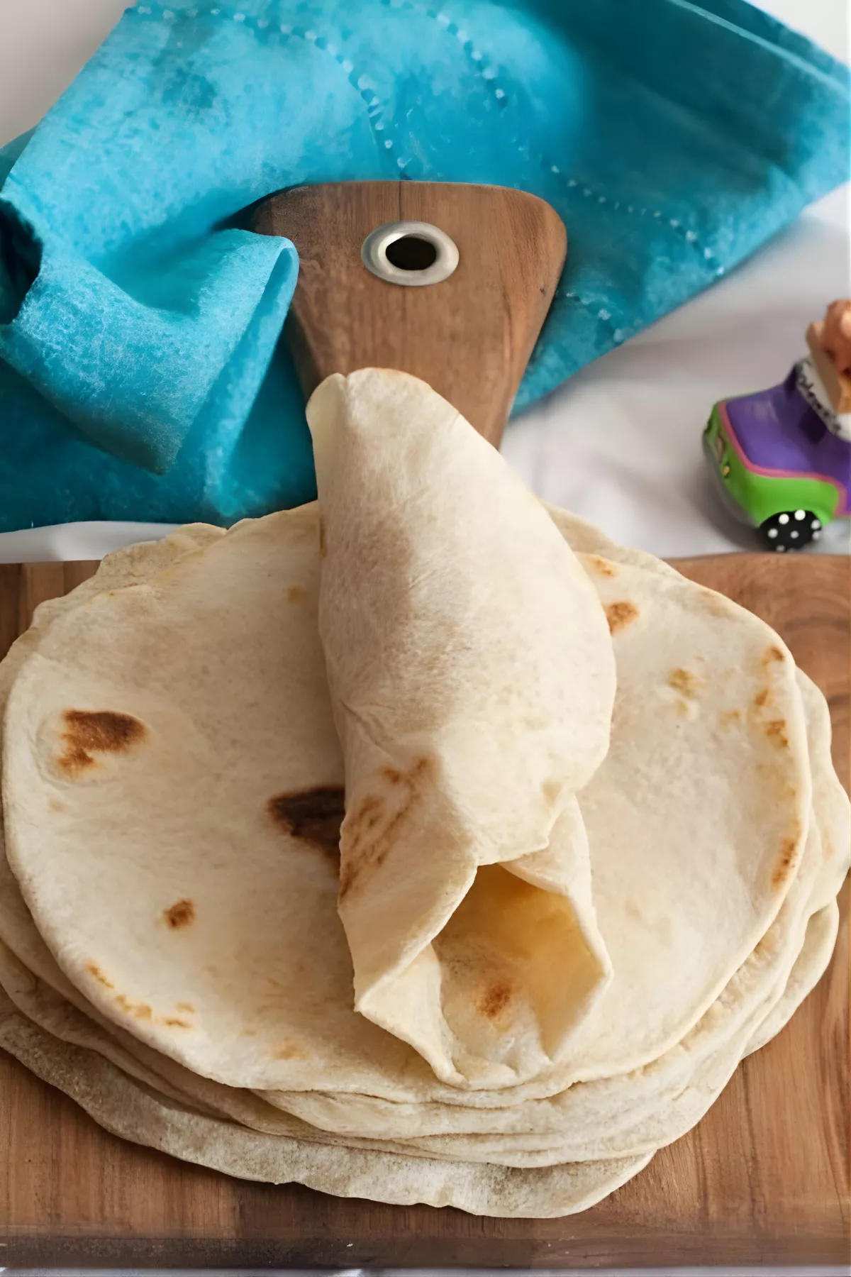 A stack of soft low FODMAP tortillas on a wooden board with a teal napkin.