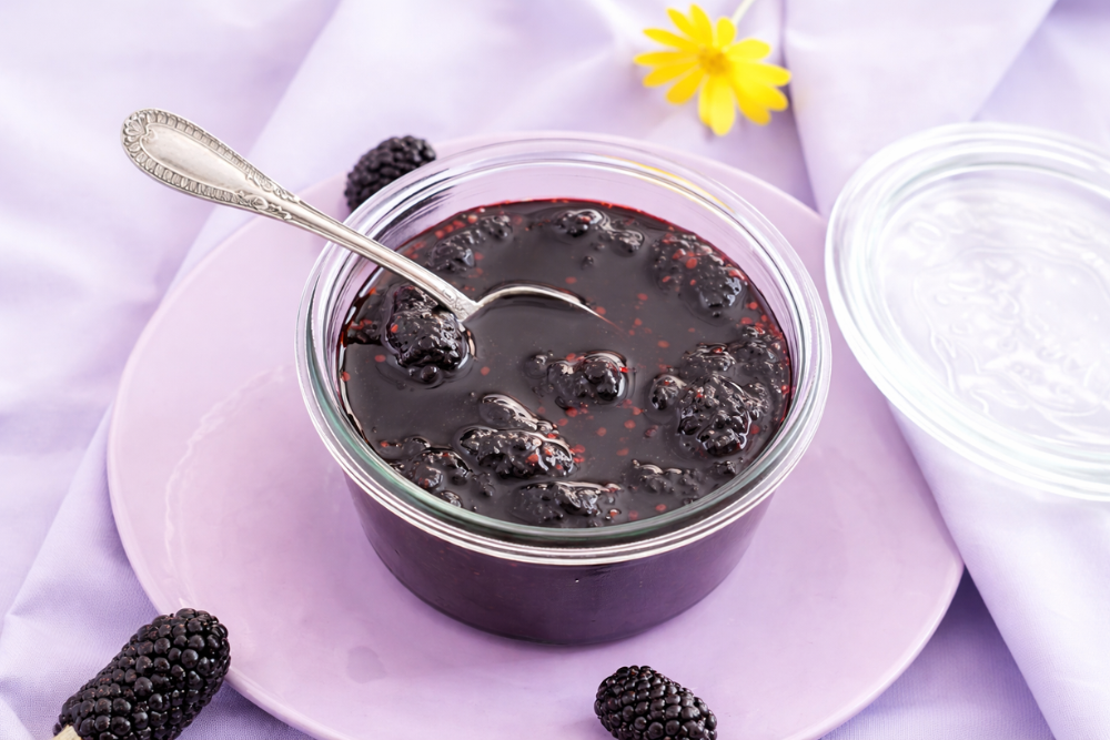 Homemade mulberry jam in an open glass jar with a spoon.