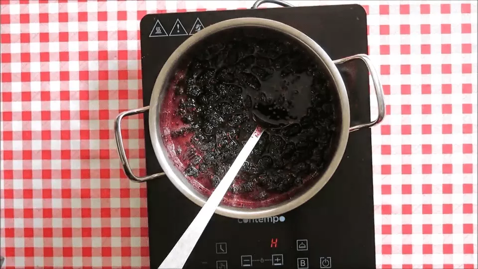 Thickened mulberry jam in the pot with a spoon.