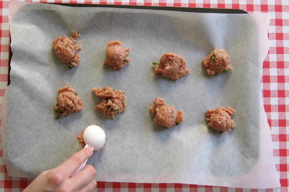 Seasoned pork mixture being portioned onto a baking tray before shaping into meatballs.