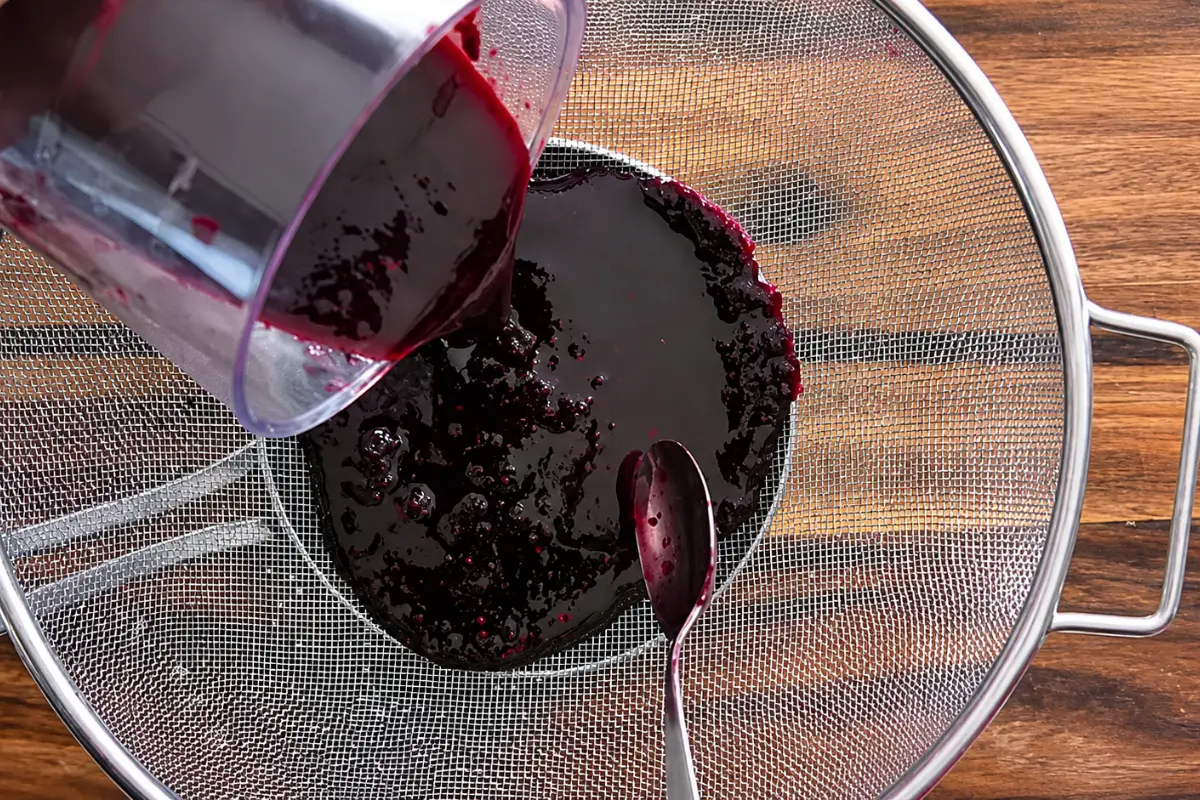 Blended mulberries being strained through a fine-mesh sieve.