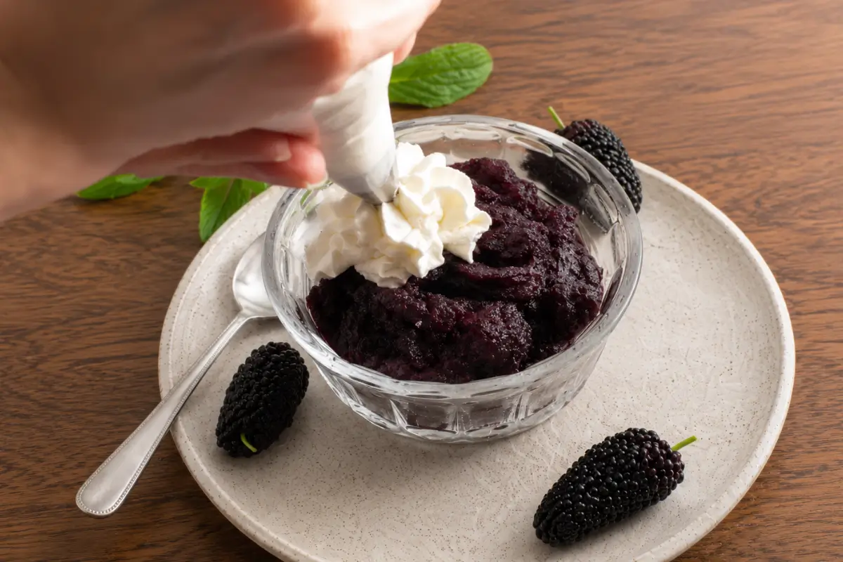 Whipped cream being piped onto the frozen berry mixture.