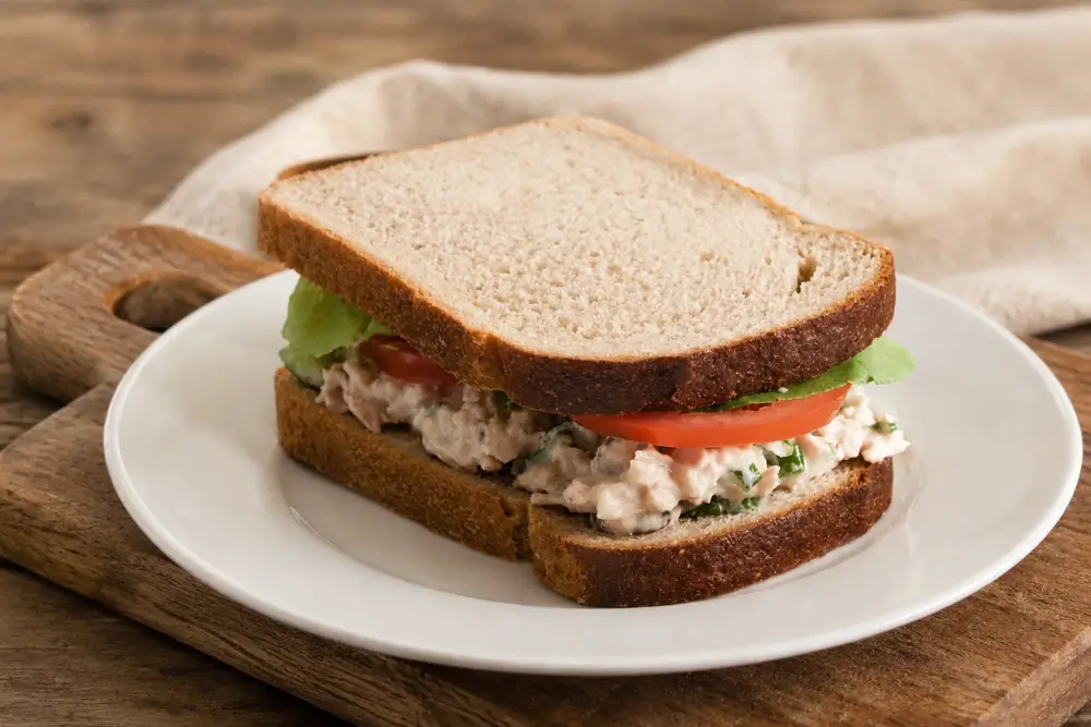Low FODMAP Tuna Salad Sandwich served on a white plate with lettuce and tomato.