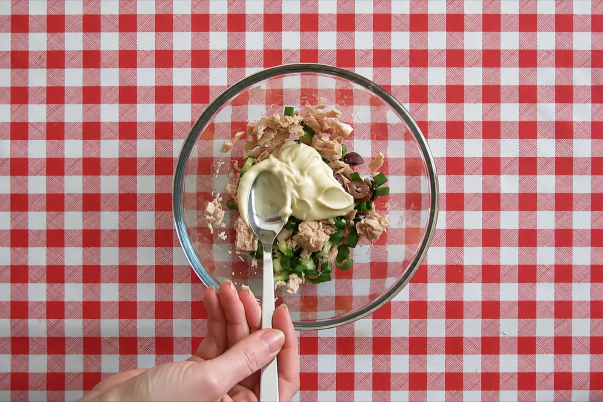 Mayonnaise being added to tuna, cucumber, green onion, and olives before mixing the tuna salad filling.