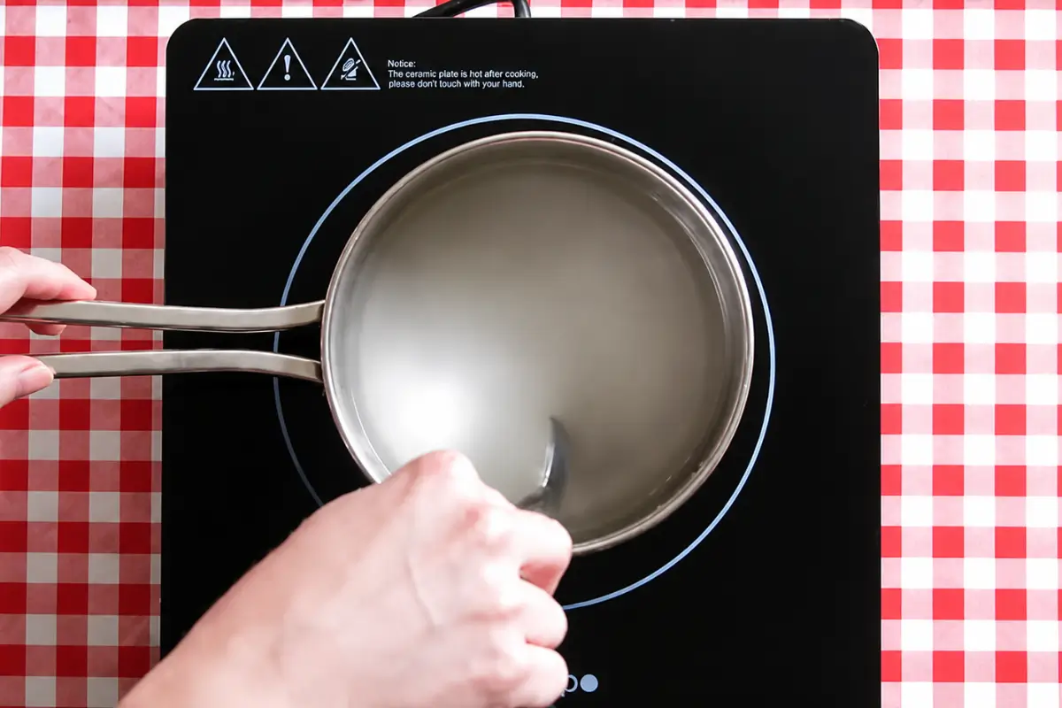 Sugar and water being stirred together in a saucepan.