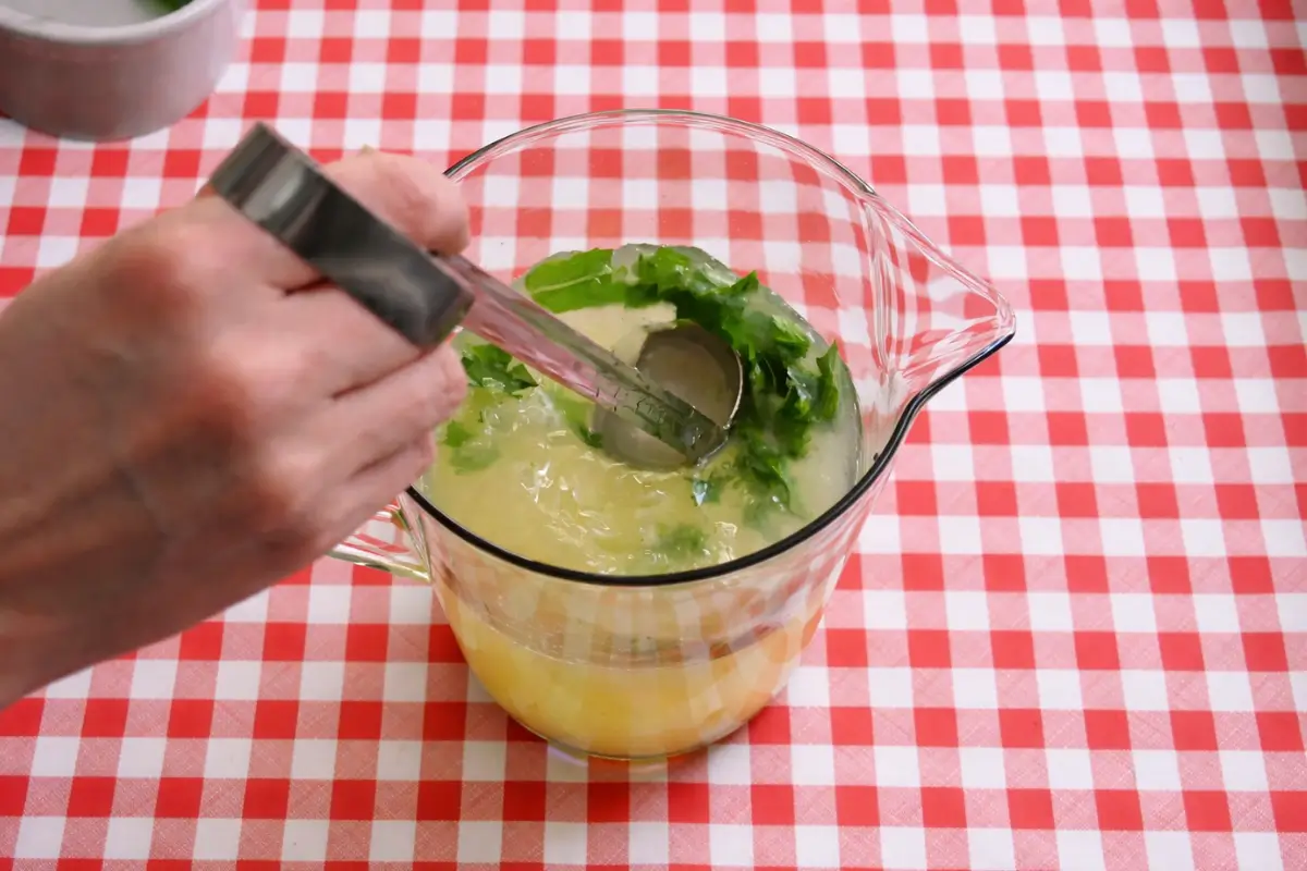 Lemon juice and mint being mixed in a jug with a spoon.