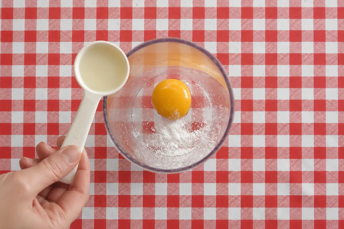 Egg yolk, salt, and oil in a blender container before mixing Low FODMAP mustard mayo.