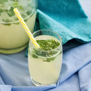 Glass of low FODMAP mint lemonade with fresh mint leaves and a striped straw.