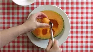Scooping melon balls from a halved rockmelon using a melon baller.