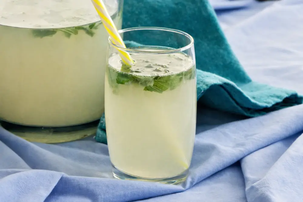Close-up of mint lemonade with mint leaves and a striped straw in a glass.