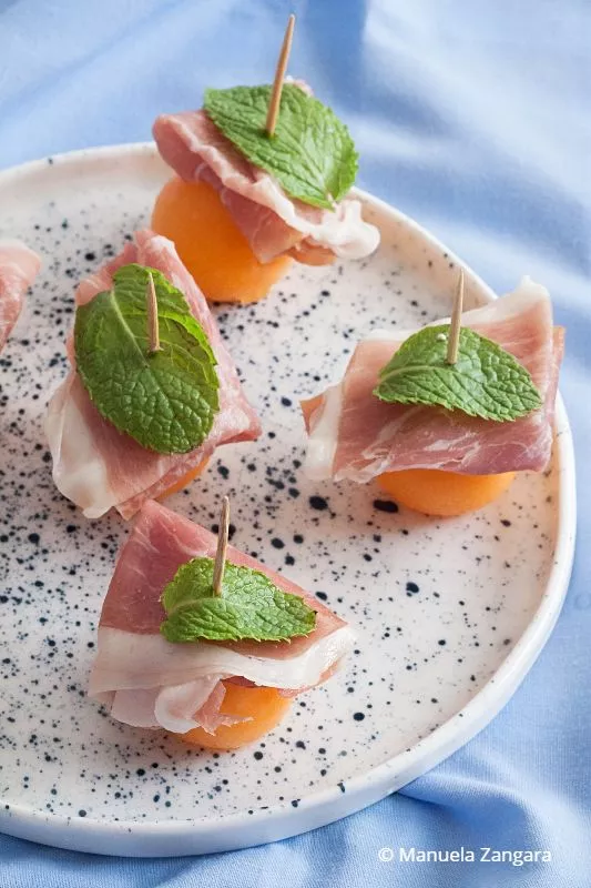 Top view of Prosciutto and Melon Bites on a plate with mint garnish.