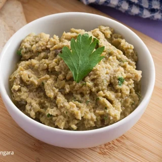 Green olive tapenade served in a white bowl garnished with fresh parsley on a wooden board.