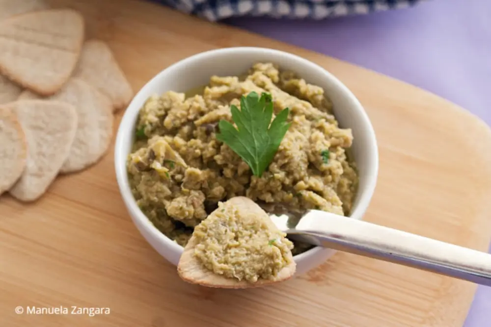 Spoon spreading olive mixture onto a small cracker.
