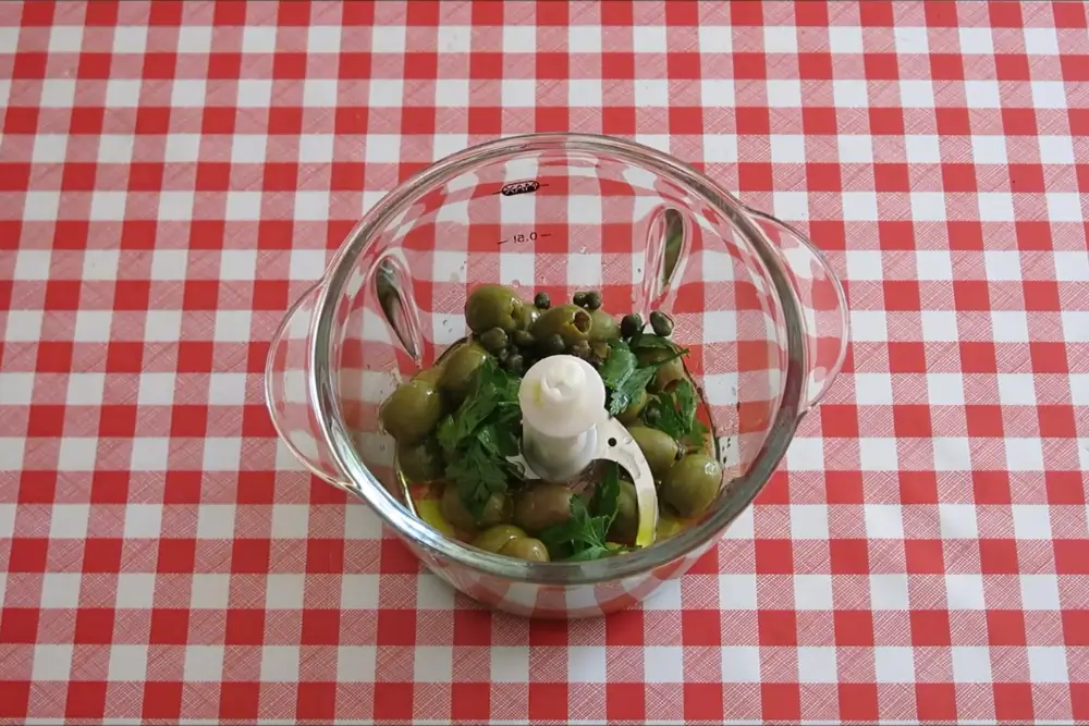 Green olives, parsley, capers and olive oil placed in a food processor before blending.