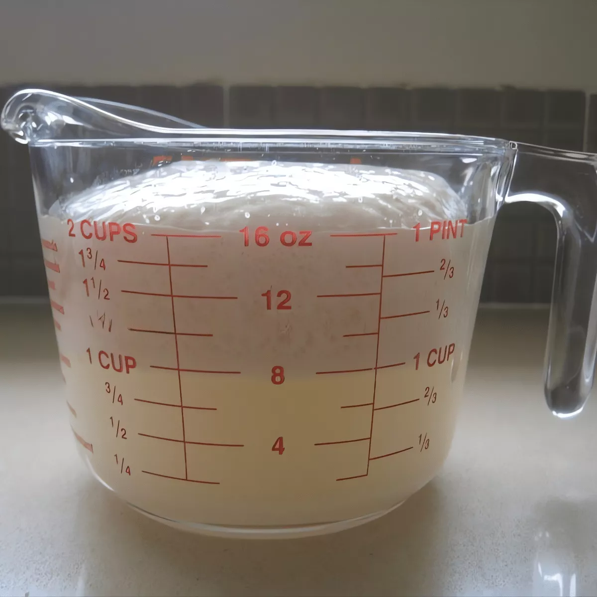 Frothy yeast mixture in a measuring cup for homemade pizza dough.
