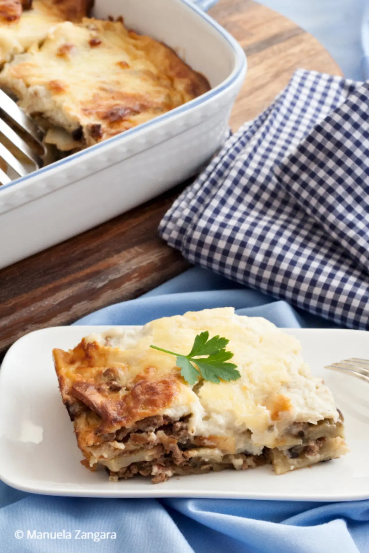 Close-up of baked moussaka in ceramic dish with golden cheese topping.