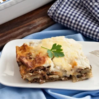 Portion of baked moussaka garnished with parsley on white plate.