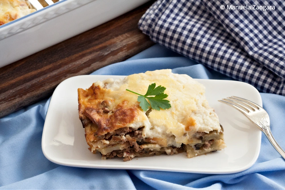 Portion of baked moussaka garnished with parsley on white plate.
