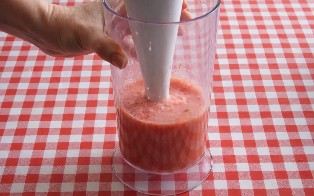 Fresh tomatoes being blended into a smooth purée in a tall container.