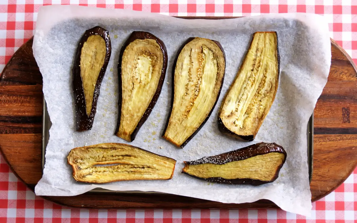 Roasted eggplant halves arranged on lined baking tray.