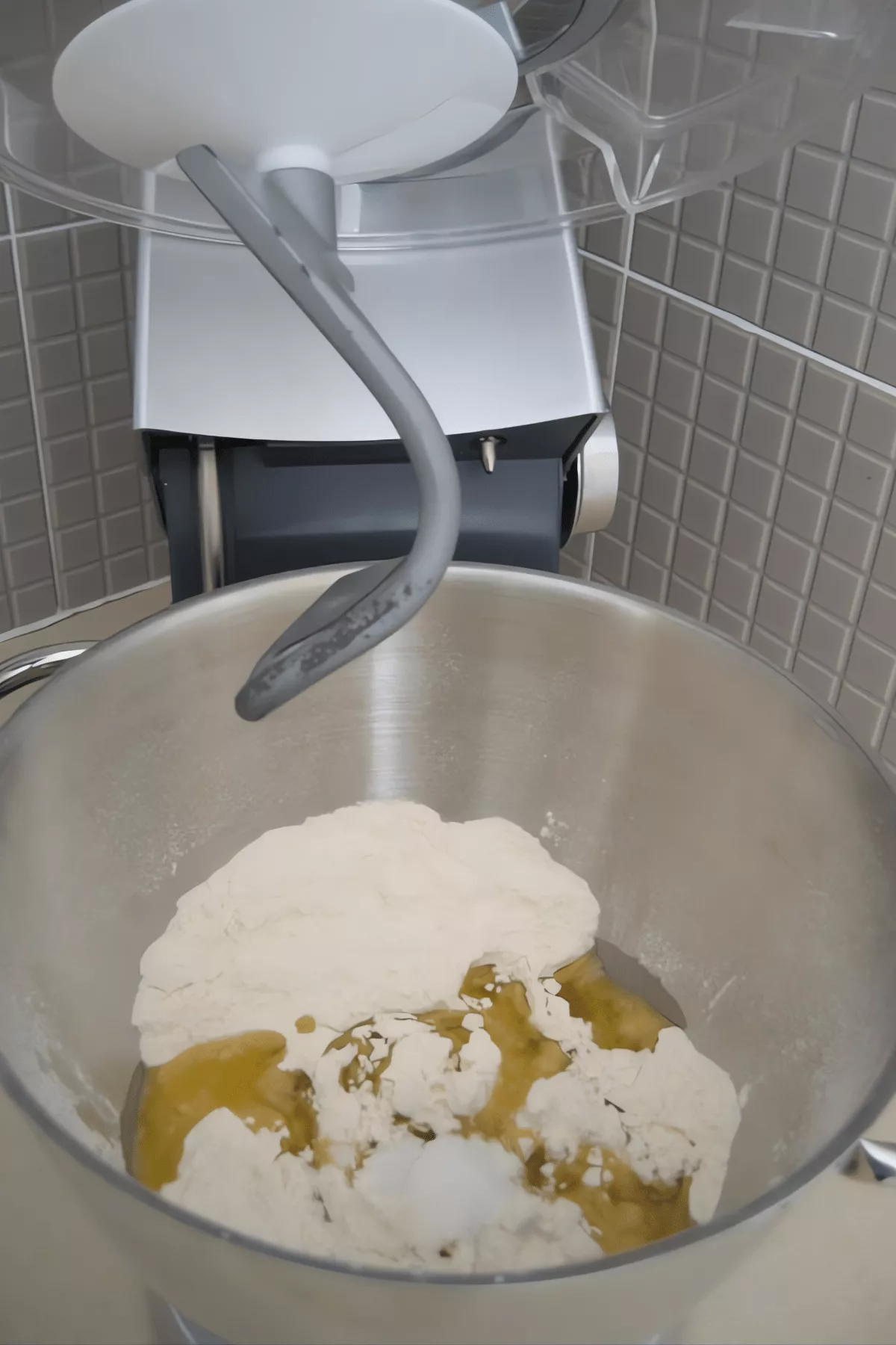 Homemade pizza dough ingredients in a mixer bowl with flour, salt and olive oil.