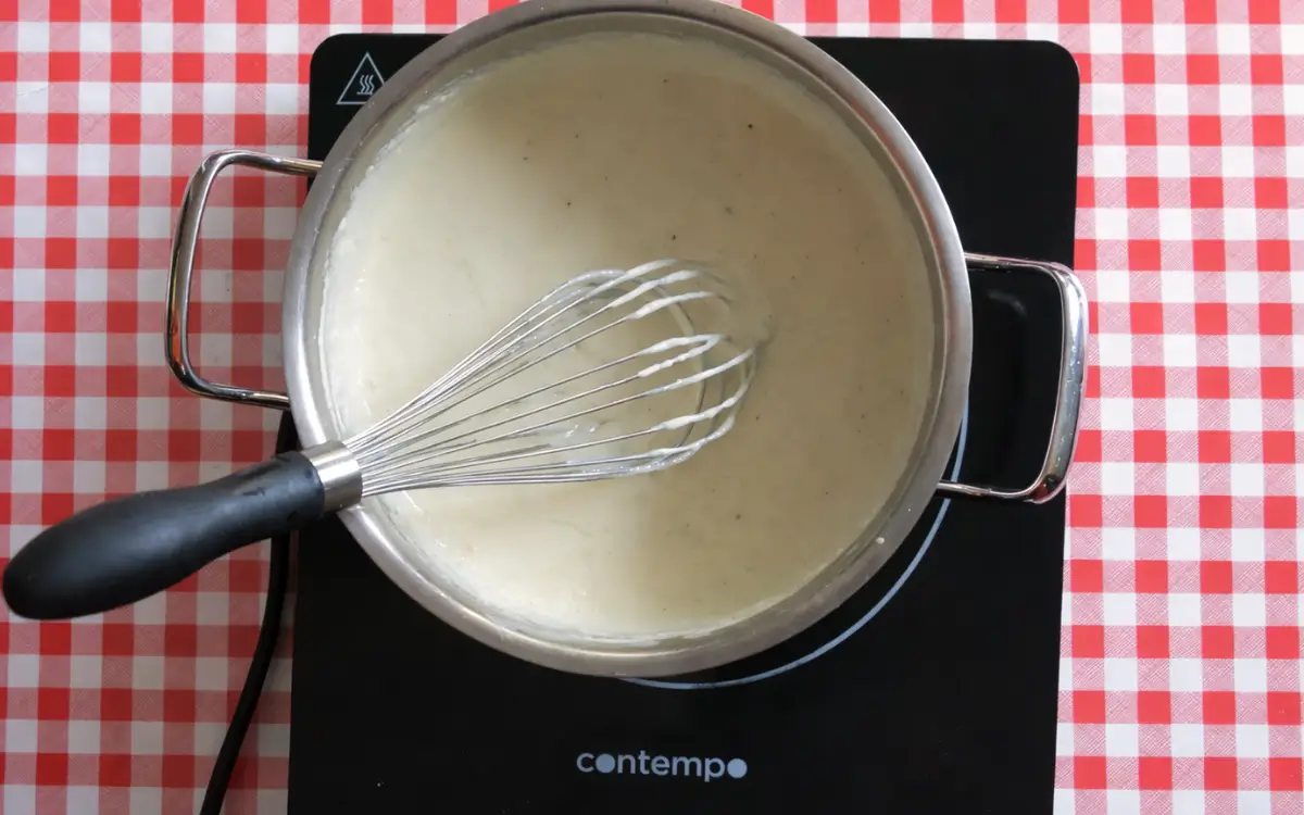 Creamy white béchamel sauce being whisked in a saucepan.