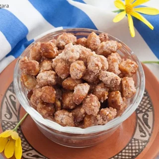 Close-up of sweet caramelised peanuts in a glass bowl with yellow flowers in the background.