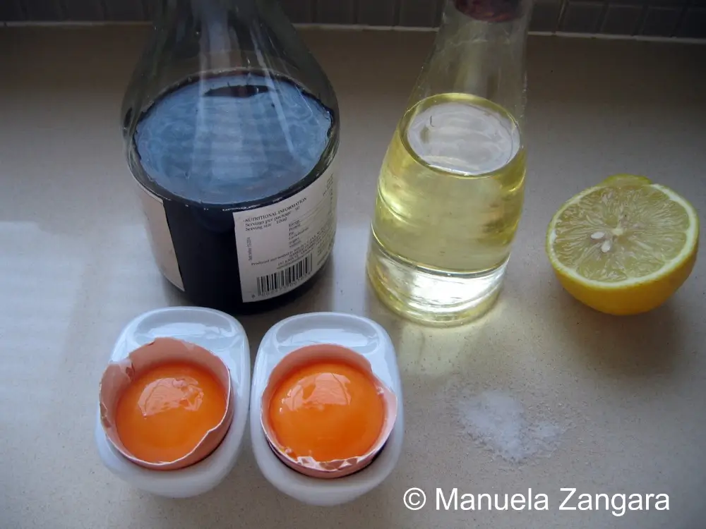Egg yolks, lemon half, vinegar, and oil placed together on a kitchen counter.