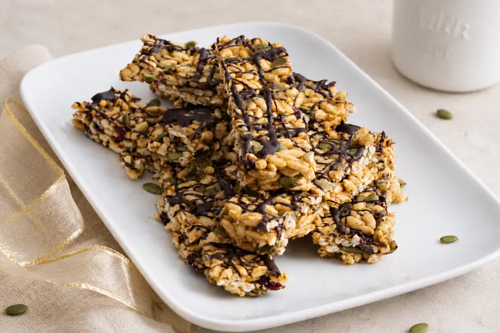 No-Bake Energy Bars with pepitas, dried cranberries and dark chocolate drizzle on a white platter.