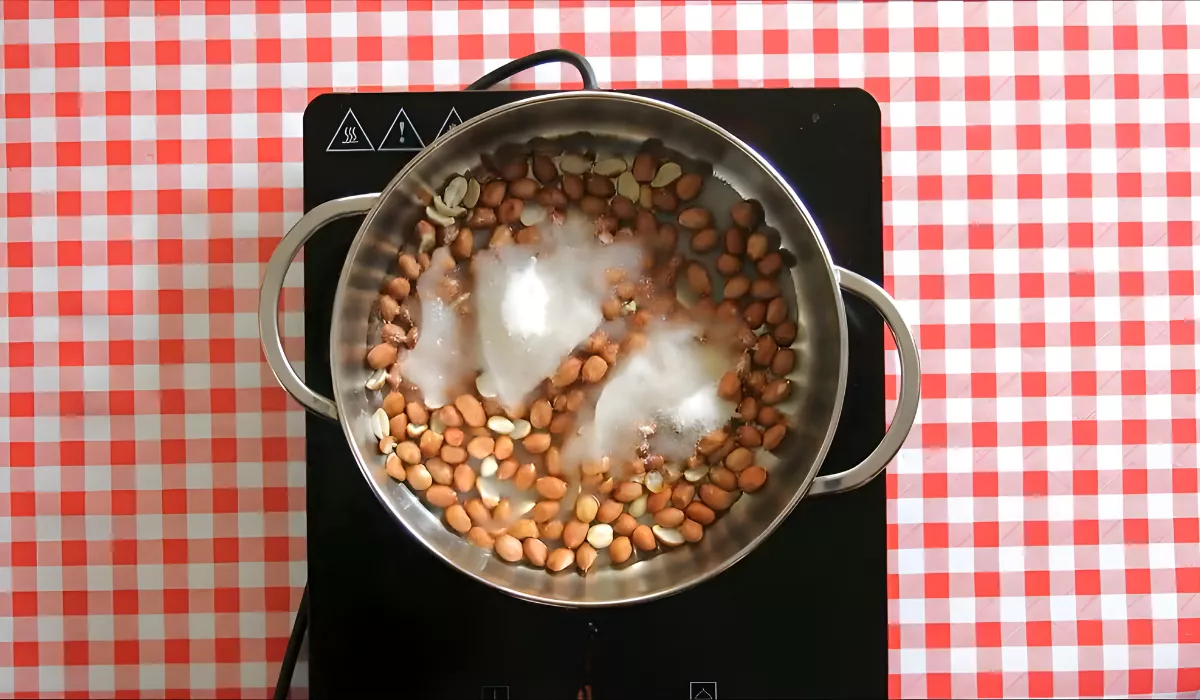 Peanuts, sugar, and water cooking in a pan on a checkered tablecloth.