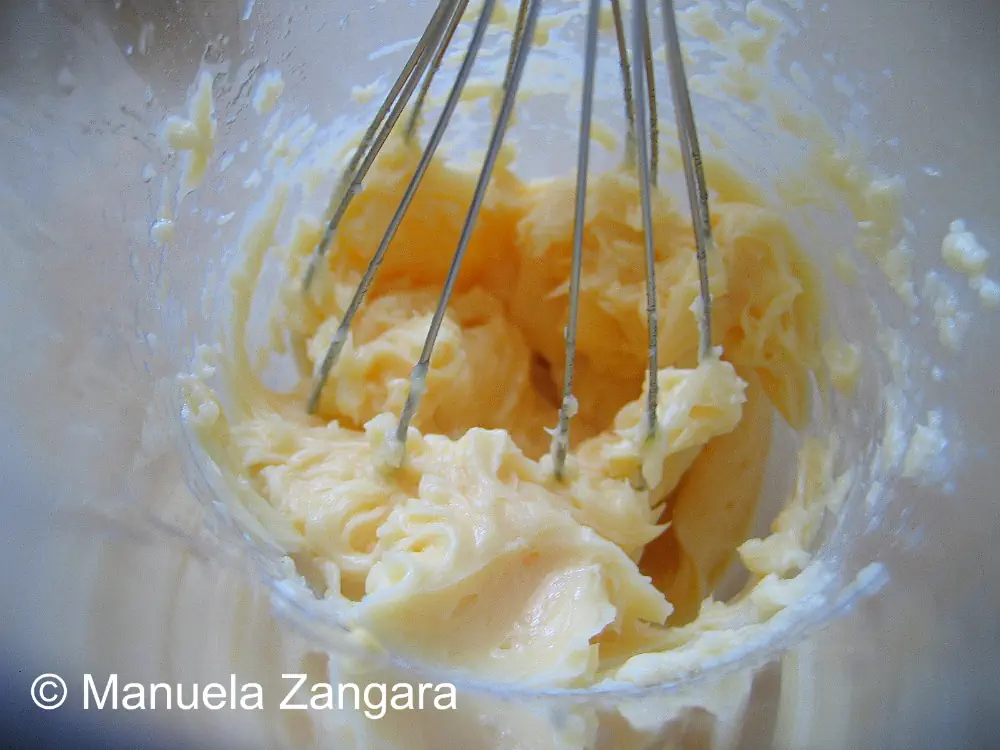 Thick, pale yellow mayonnaise forming around the whisk inside the mixer.