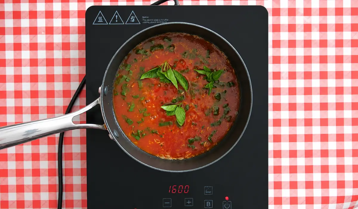 Basil leaves simmering over tomato rice in a saucepan.