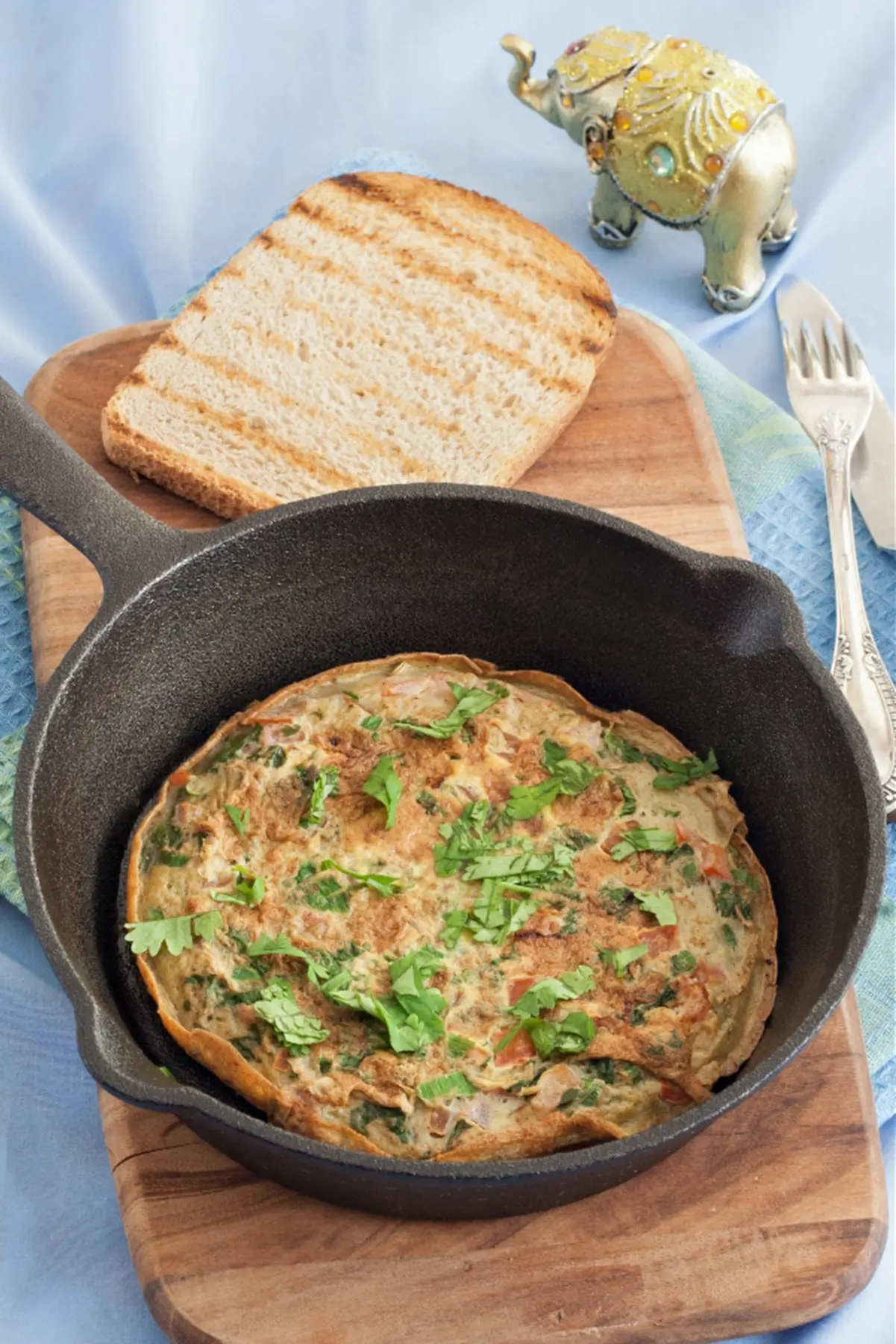 Cooked Indian-style omelette served with toasted bread and fresh lime in a cast iron skillet.