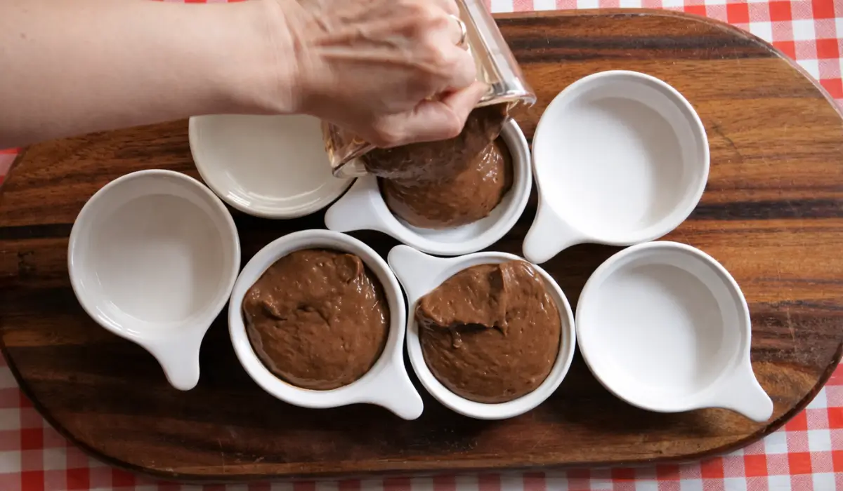 Pouring thick chocolate custard into small white ramekins.