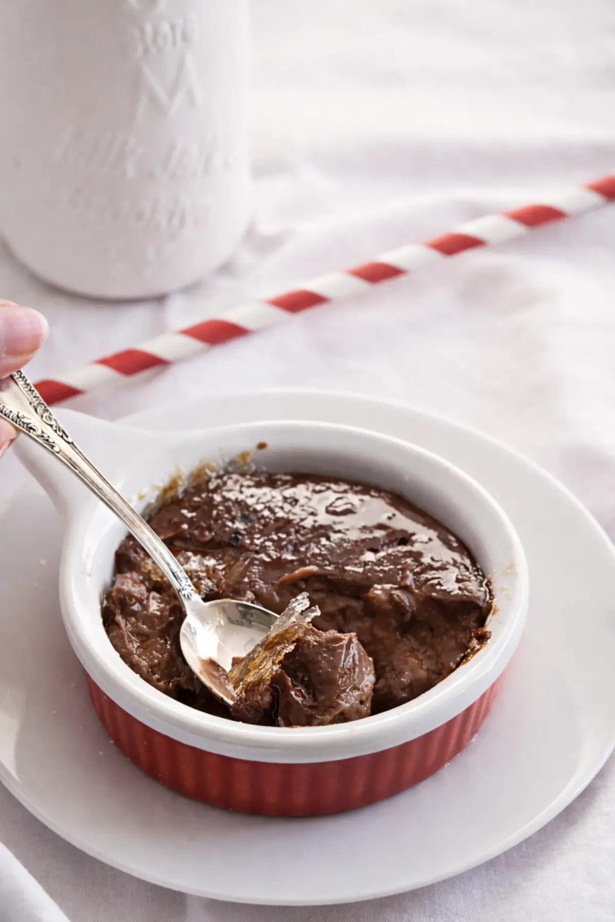 Spoon lifting caramel shards and creamy chocolate custard from a red ramekin.