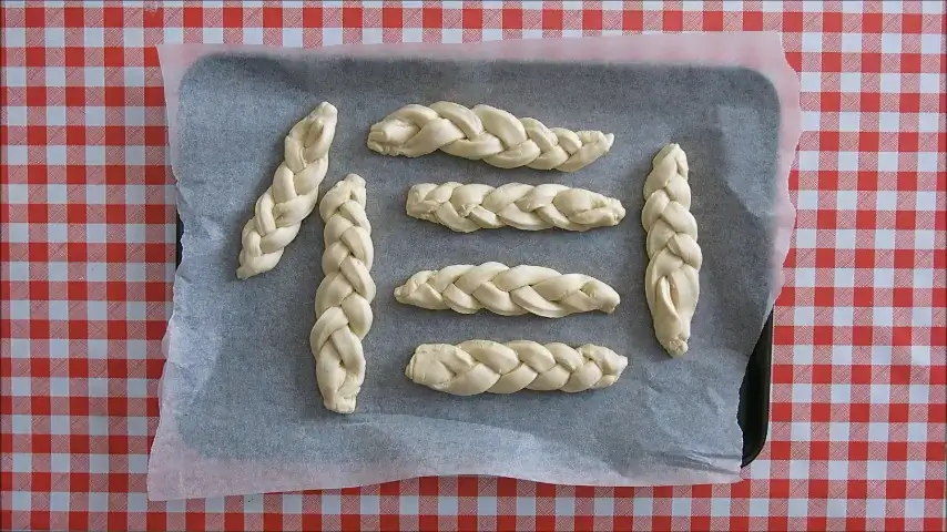 Braided koeksisters dough pieces resting on parchment before frying.
