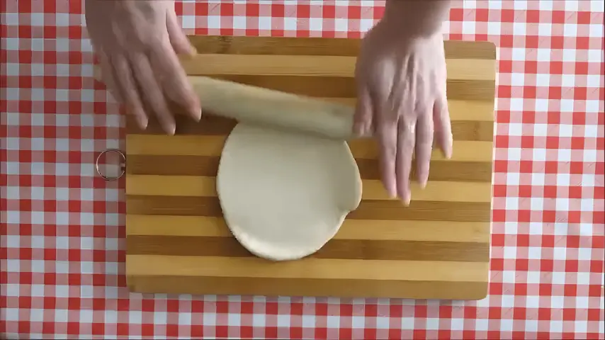 Hands rolling out koeksisters dough evenly on a wooden board.