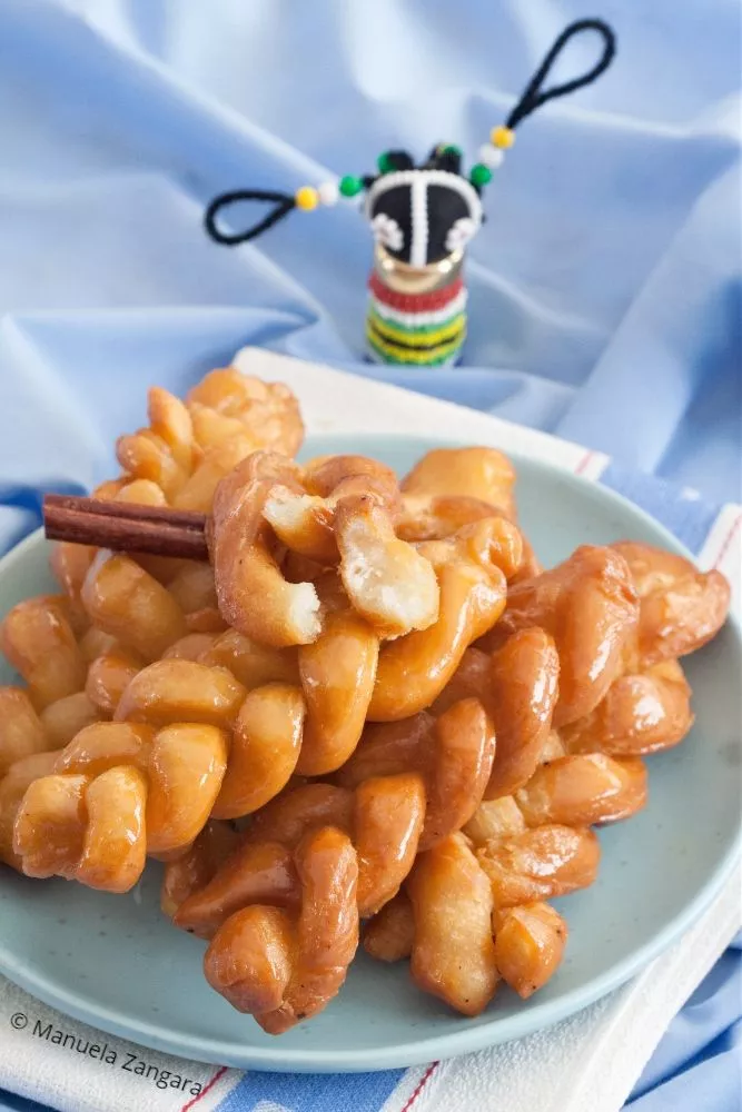 Traditional South African koeksisters stacked on a plate with a blue background.