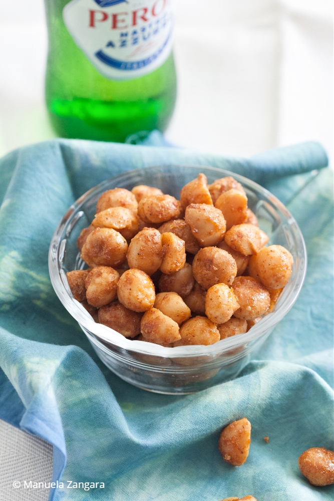 Bowl of sweet and spicy macadamia nuts served with a bottle of beer.