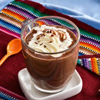 Mexican Hot Chocolate topped with whipped cream and chilli flakes in a glass mug.
