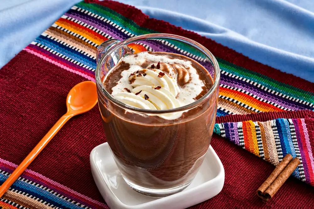 Mexican Hot Chocolate topped with whipped cream and chilli flakes in a glass mug.