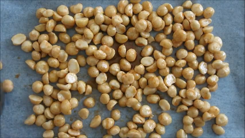 Coated macadamia nuts spread on a baking tray before roasting.