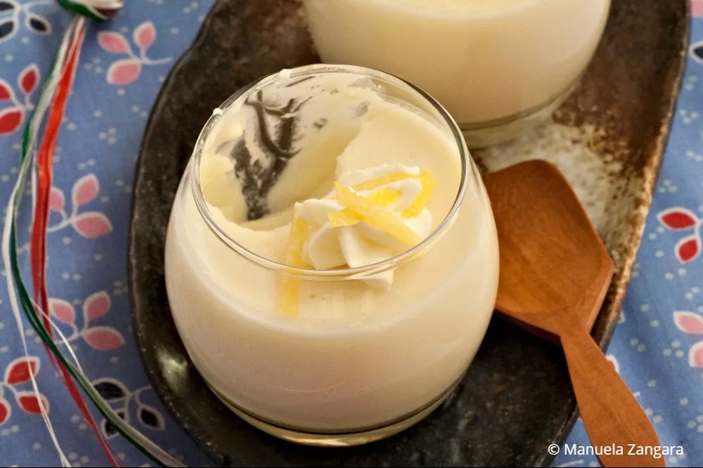 Glass of creamy Lemon Panna Cotta topped with whipped cream and lemon zest.
