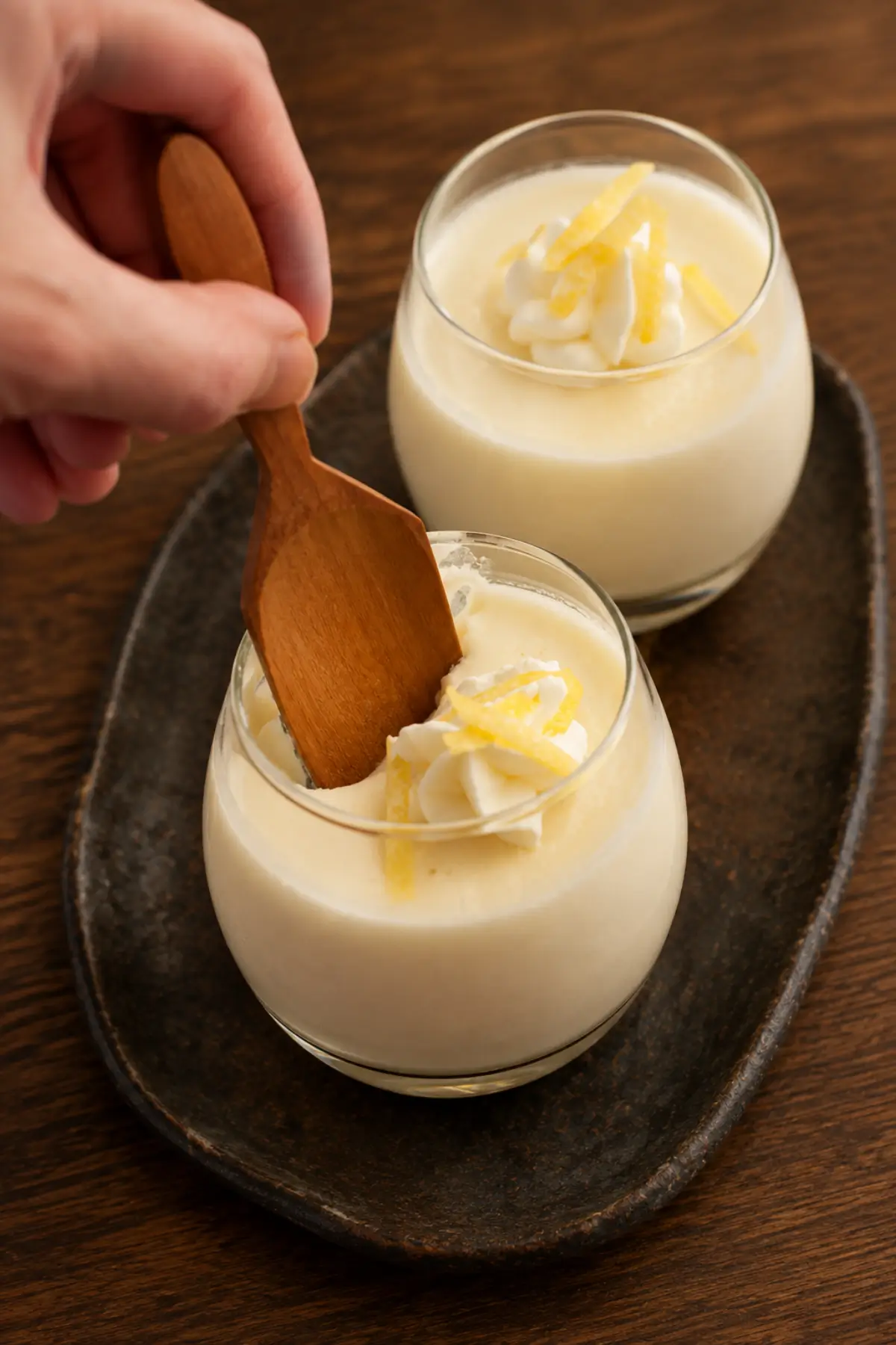 Two dessert glasses topped with whipped cream and strips of lemon zest.