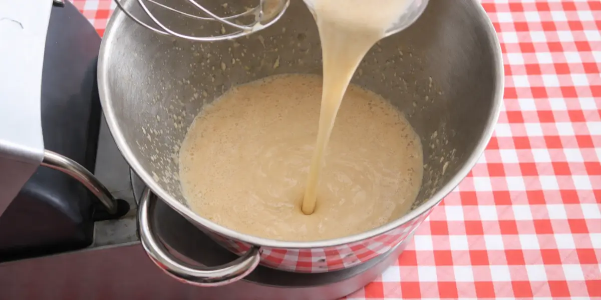Milk being poured into the whisked coffee and egg mixture in a metal bowl.