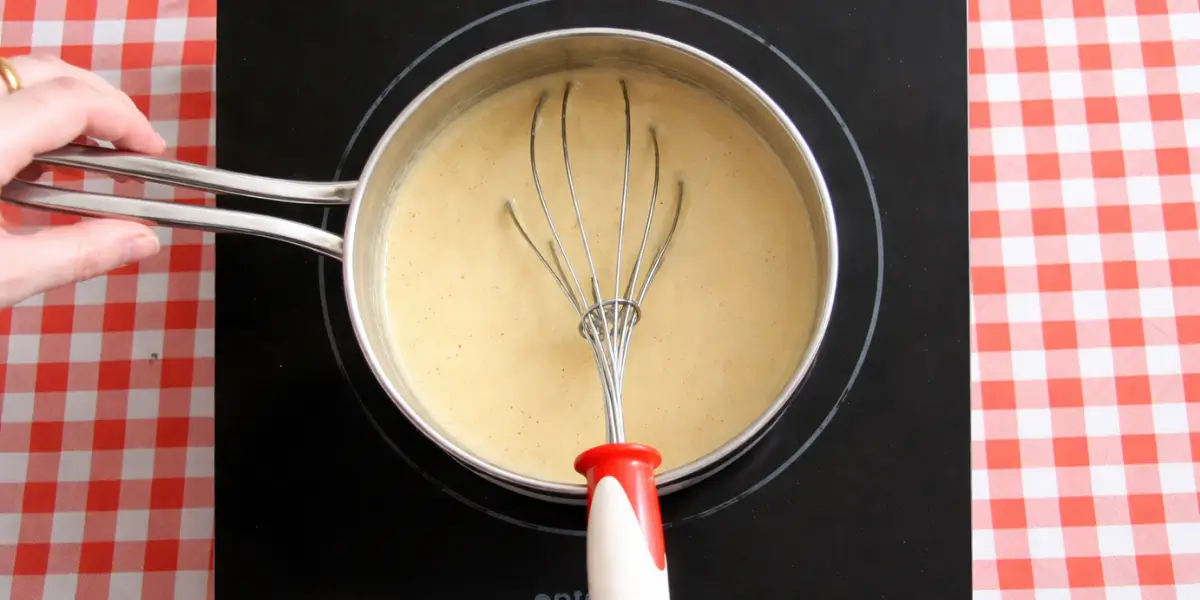 Coffee custard thickening in a saucepan while being whisked over medium heat.