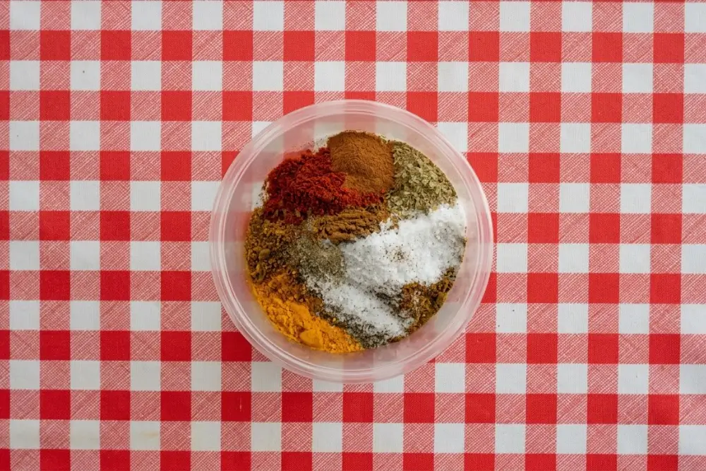 Measured ground spices and salt layered in a plastic container before mixing.