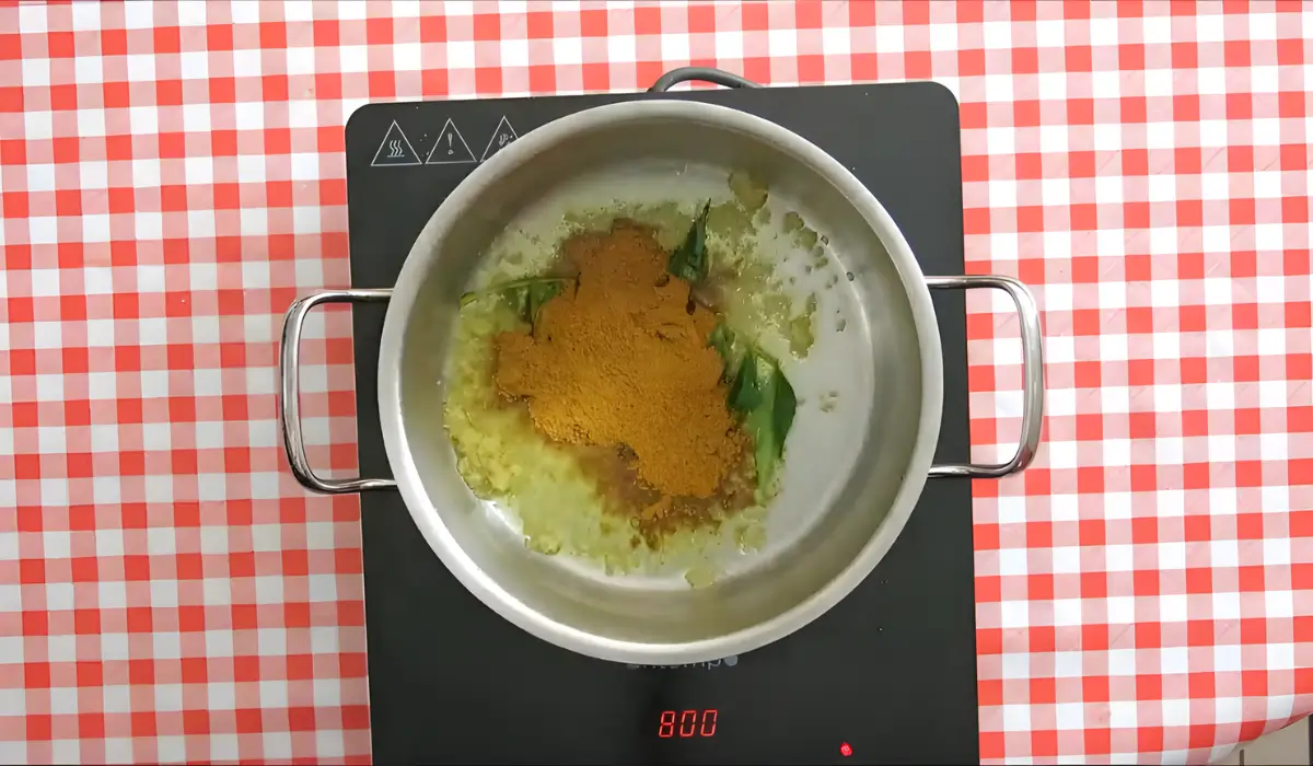 Curry spices frying with ginger and curry leaves in a pot.