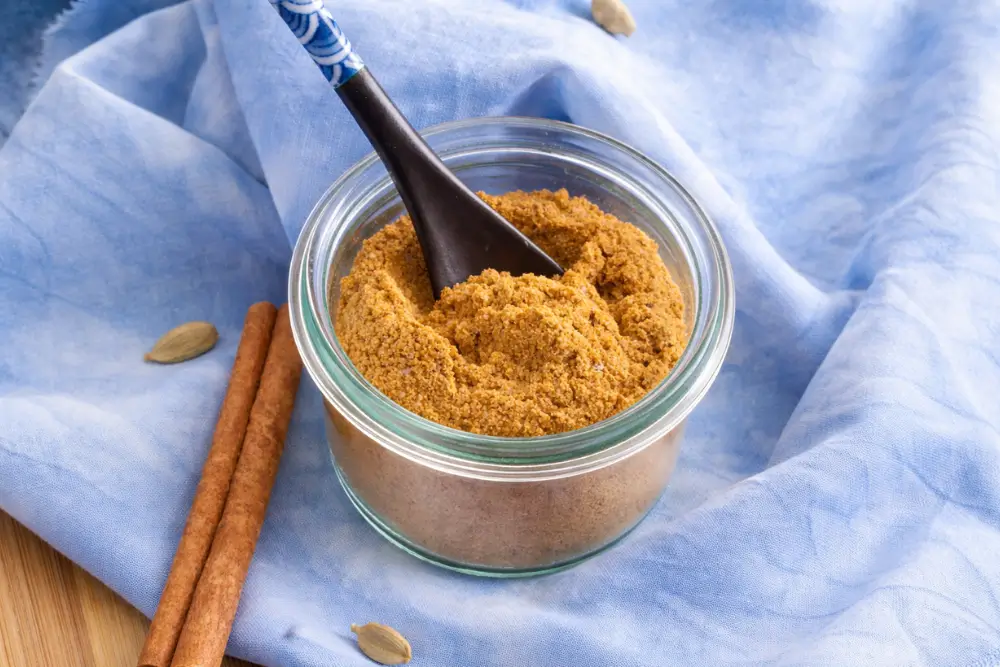 Golden curry spice blend in a glass jar with cinnamon sticks beside it.