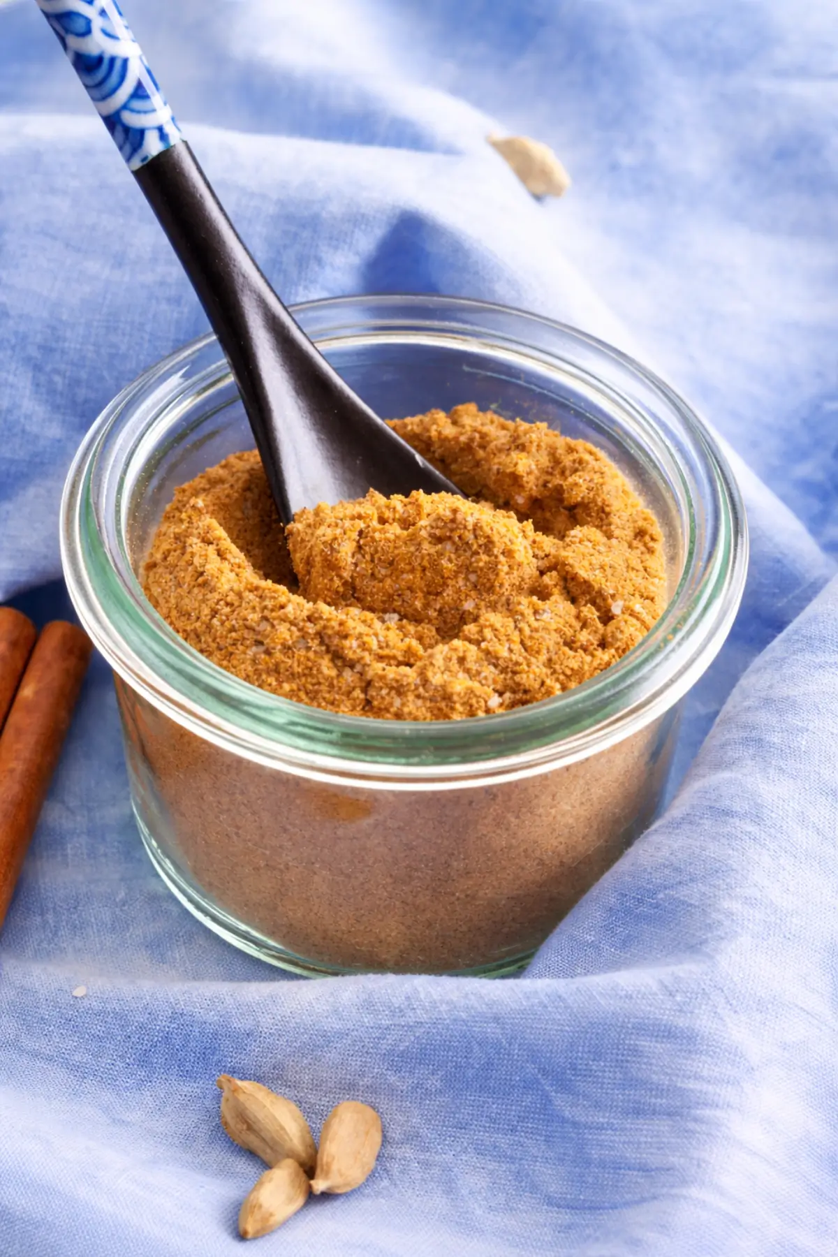 Low FODMAP curry spice mix in a glass jar with a spoon and cardamom pods.
